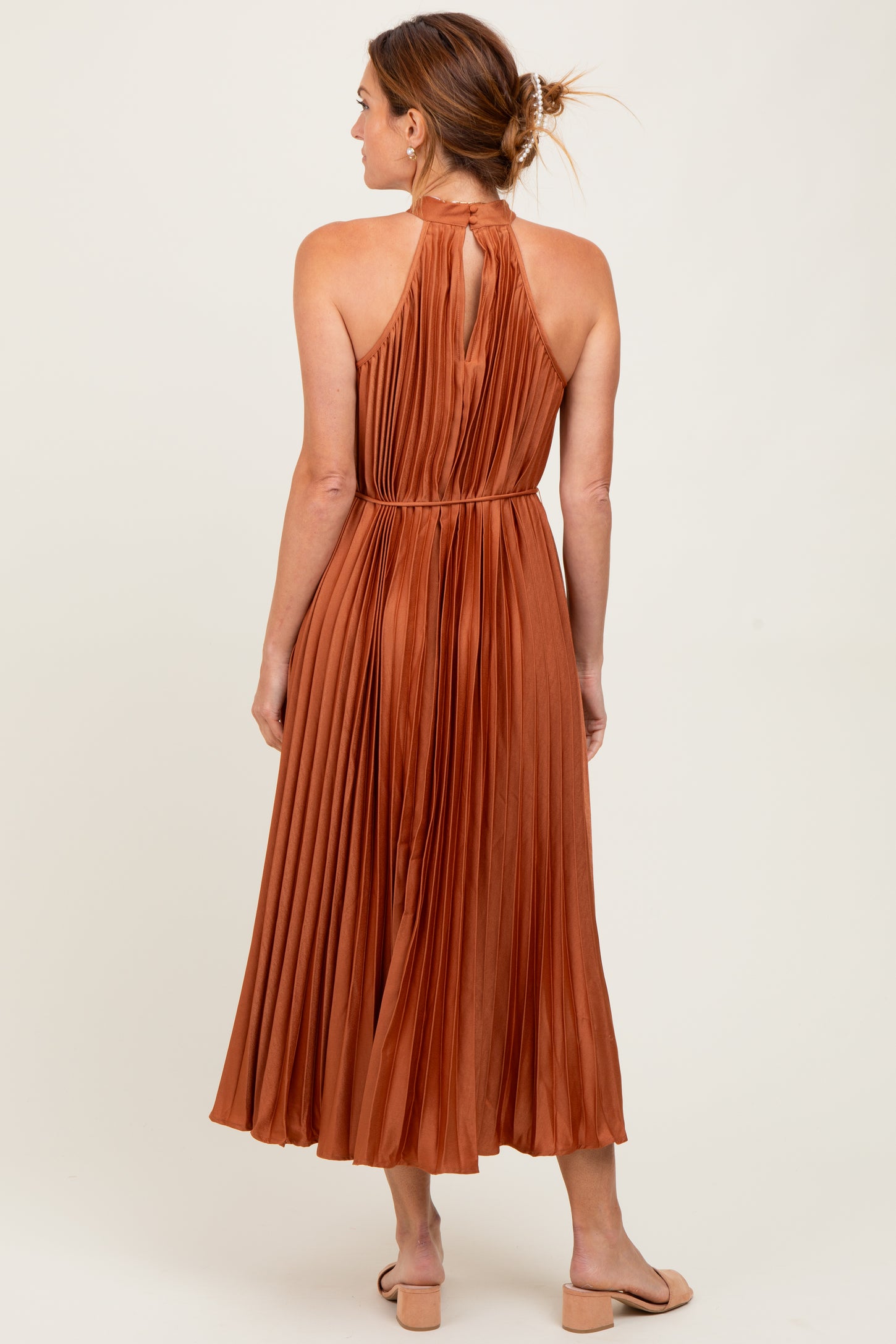 woman wearing a rust-colored pleated halter neck maxi dress, showing the back view and a flowing skirt
