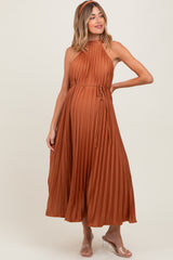 woman wearing a rust pleated maternity dress with a tie waist and halter neckline, showing her baby bump