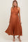 woman wearing a rust pleated maternity dress with a halter neck and a tied waist, showcasing her baby bump