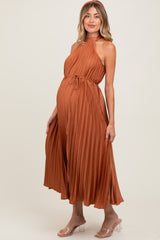 woman wearing a rust pleated maternity dress with a halter neck and adjustable tie, showcasing her baby bump.