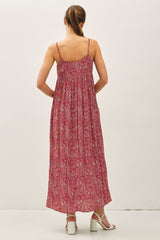 woman wearing a long red patterned maxi dress with thin straps, shown from the back