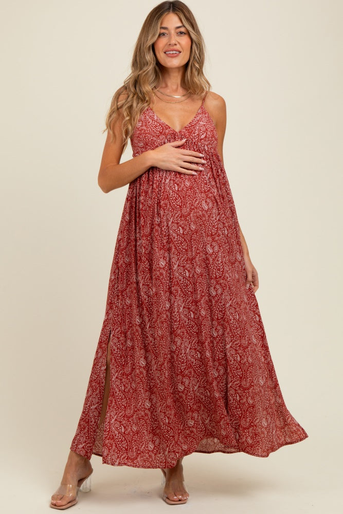 woman wearing a red patterned maternity maxi dress with a loose fit and side slits, holding her baby bump