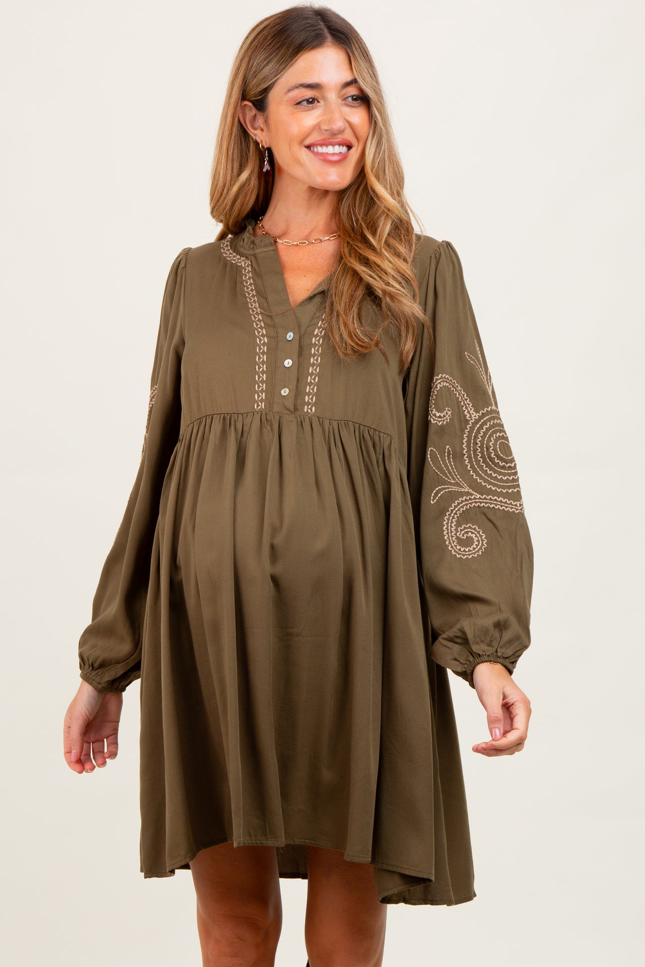 woman wearing an olive green maternity dress with embroidery and a baby bump