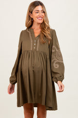 woman wearing an olive green maternity dress with embroidery and a baby bump
