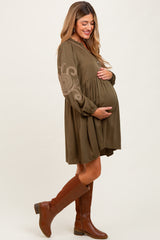 woman wearing a dark olive green maternity dress with embroidery and holding her baby bump