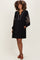 woman wearing a black maternity dress with embroidered details and long sleeves, standing with hands in pockets and showing baby bump