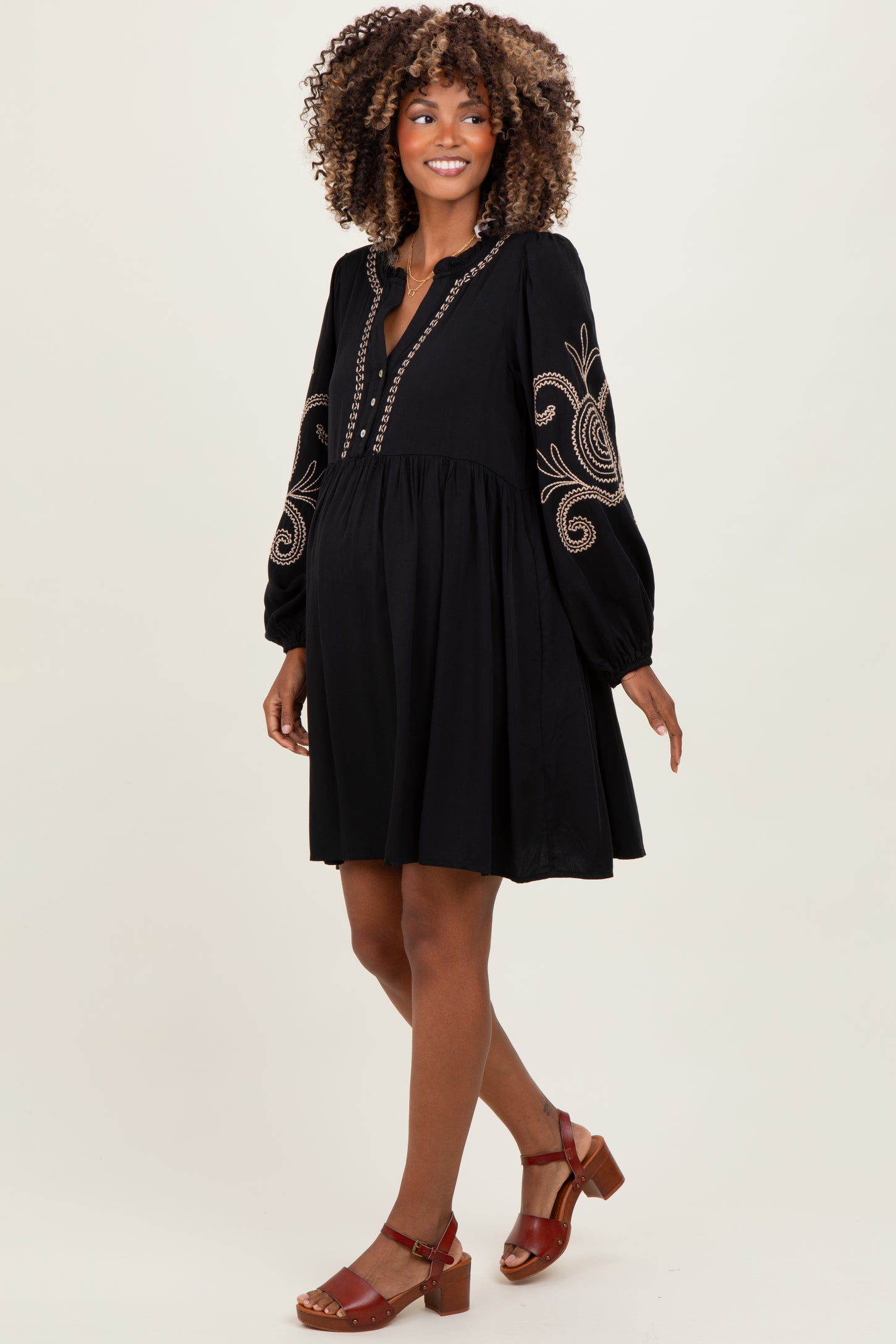 woman wearing a black maternity dress with embroidered sleeves and a flowy silhouette, showcasing a baby bump