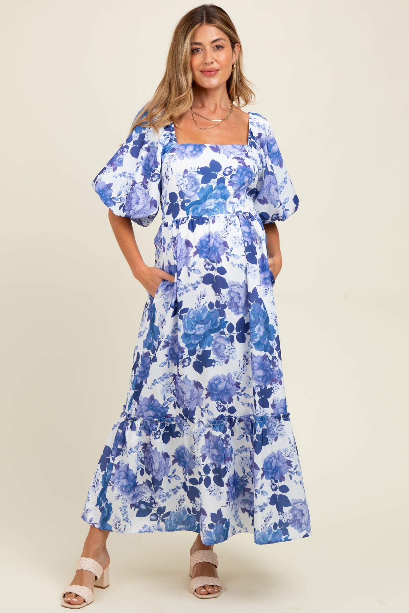 woman wearing a blue and white floral maternity maxi dress with puff sleeves and pockets, featuring a baby bump