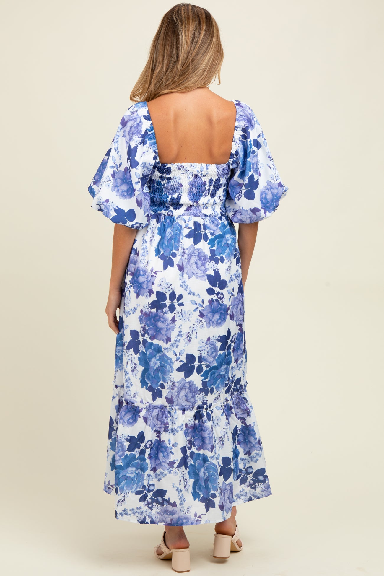woman wearing a maternity maxi dress with a blue floral print and puff sleeves, showing a beautiful back design