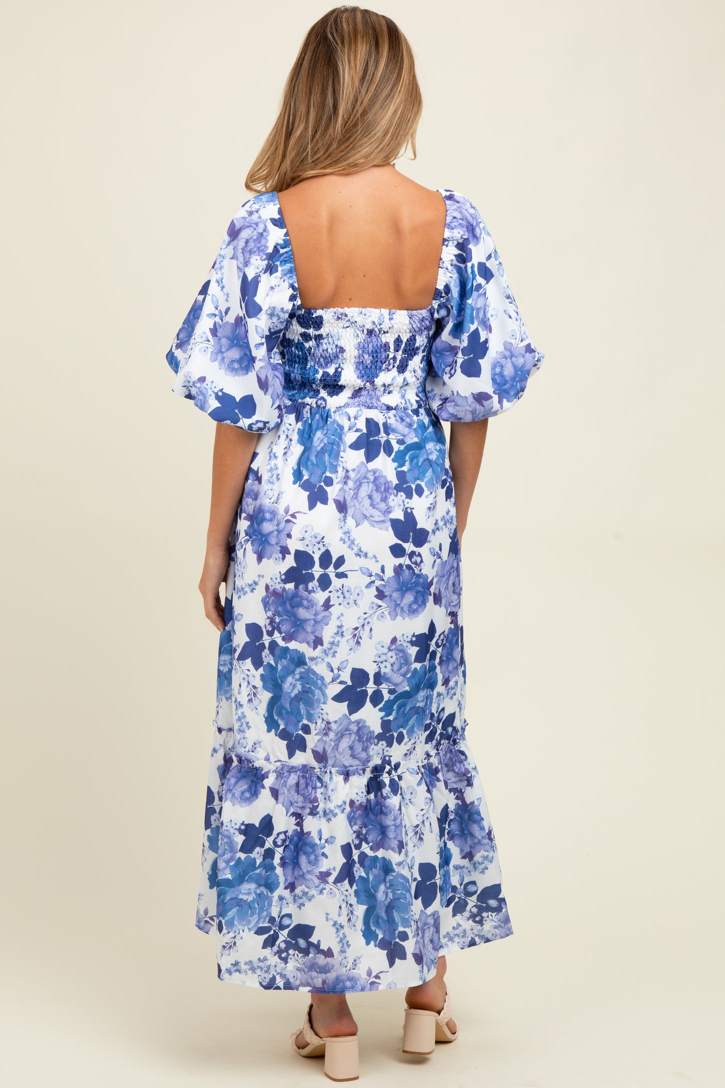 woman wearing a maternity maxi dress with a blue floral print and puff sleeves, showing a beautiful back design