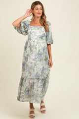 woman wearing a floral maxi maternity dress with puff sleeves and a tiered skirt, gently holding her baby bump