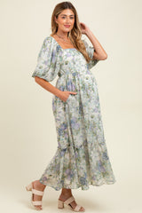 woman wearing a floral maternity maxi dress with puff sleeves and a baby bump, posing with one hand in the pocket