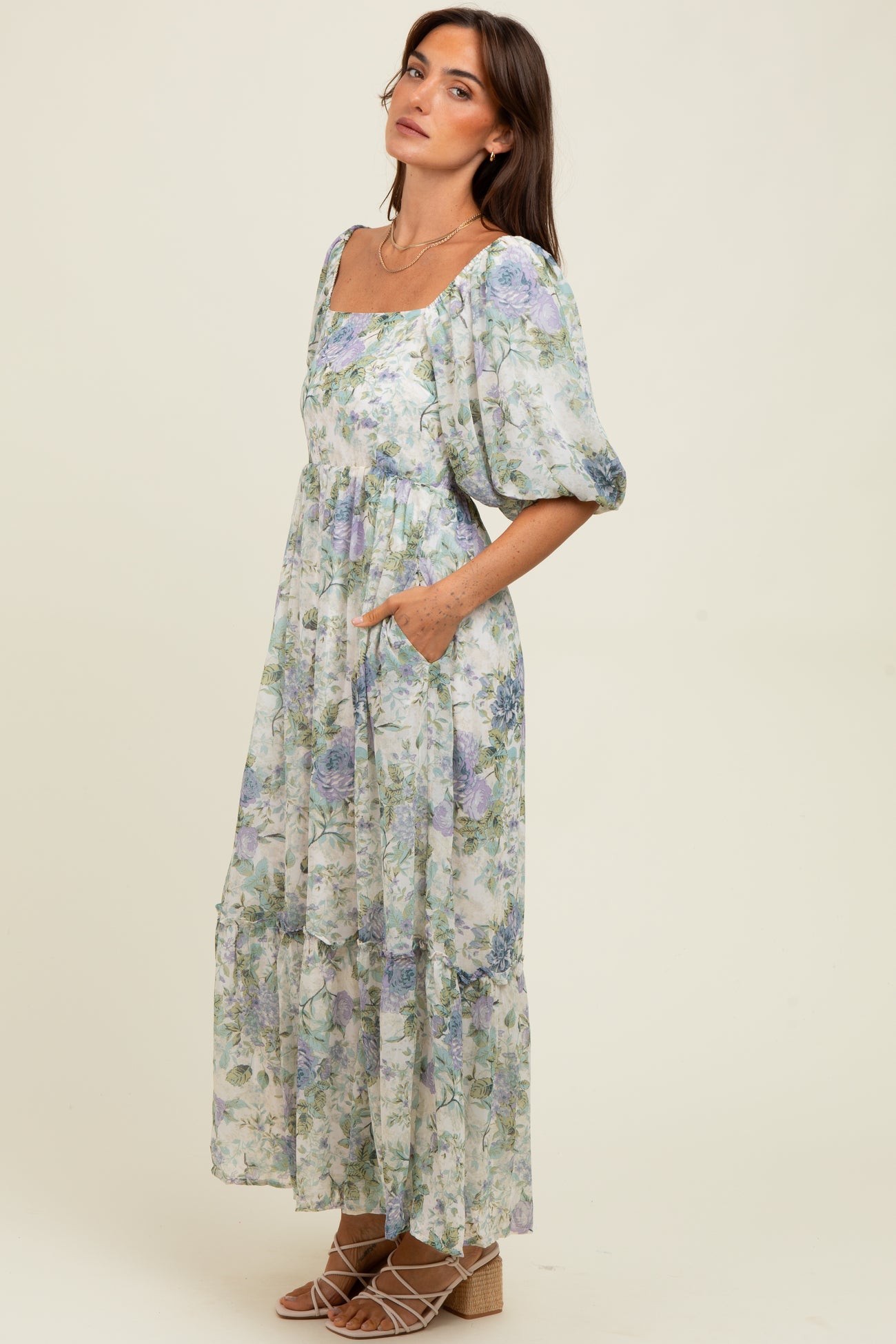 woman wearing a floral maxi dress with a square neckline, puff sleeves, and pockets