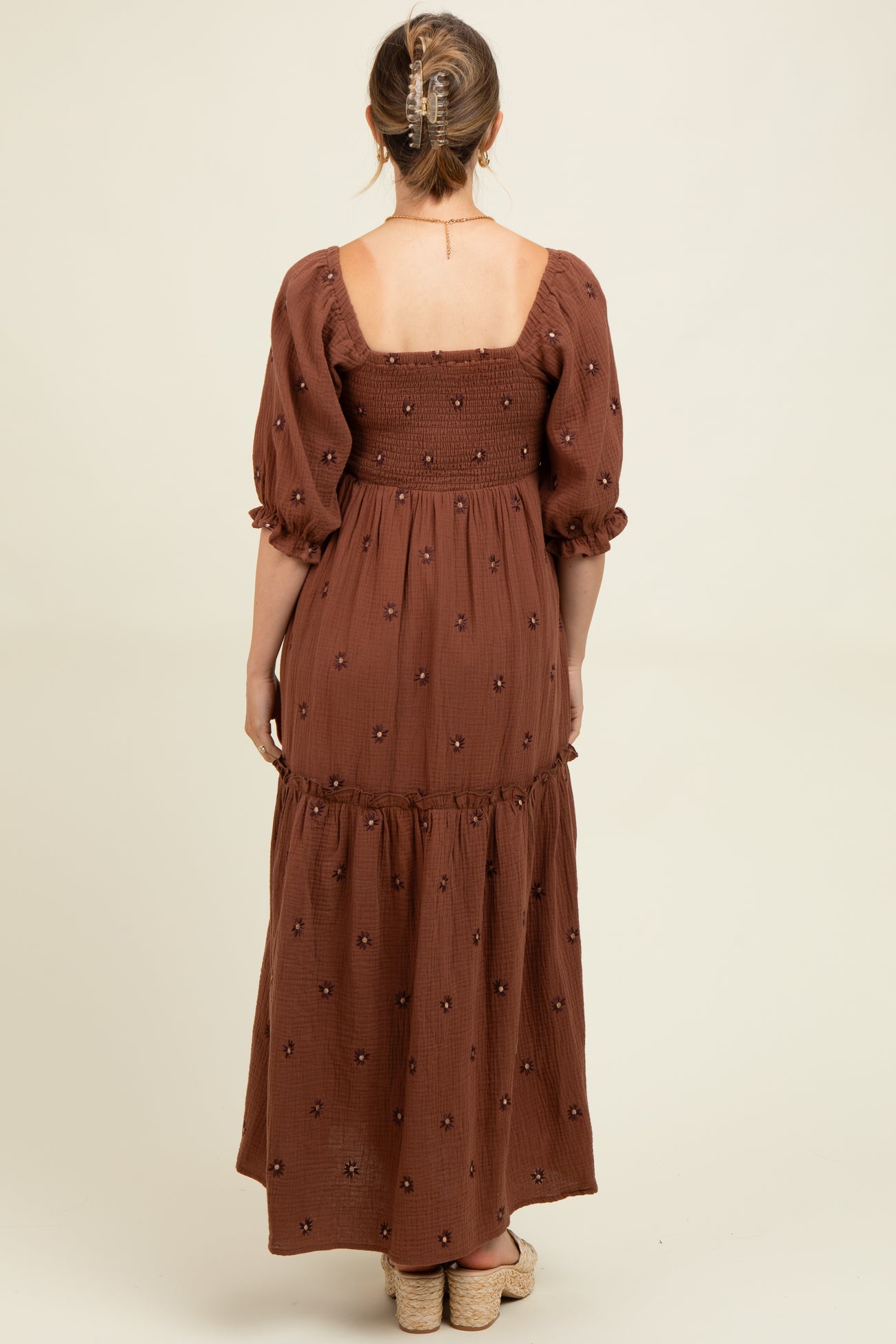 woman wearing a brown maternity maxi dress with puff sleeves and floral embroidery, showing the back view