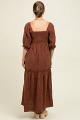woman wearing a brown maternity maxi dress with puff sleeves and floral embroidery, showing the back view