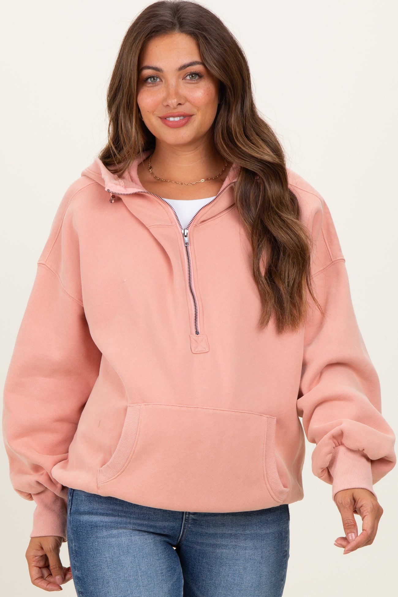 woman wearing a dusty rose maternity sweatshirt with a half-zip and front pocket, paired with blue jeans