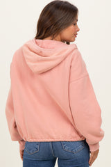 woman wearing a pink maternity hoodie with a drawstring hood and elastic hem, styled with dark jeans