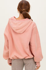 woman wearing a soft pink oversized hoodie with a drawstring hood and dropped shoulders, seen from the back