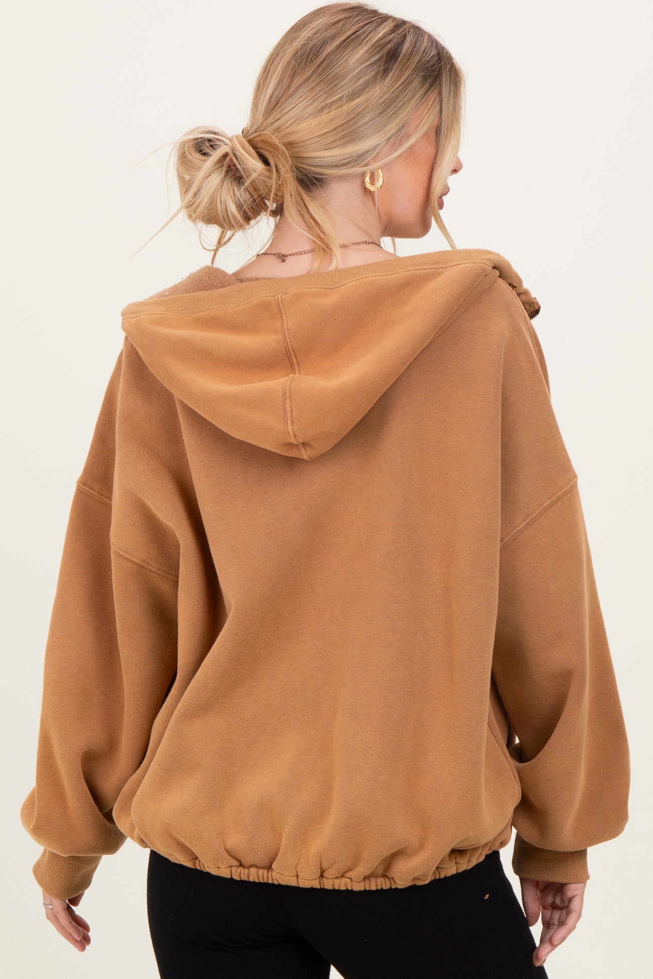 woman wearing a brown oversized hoodie with a drawstring and elastic hem, shown from the back