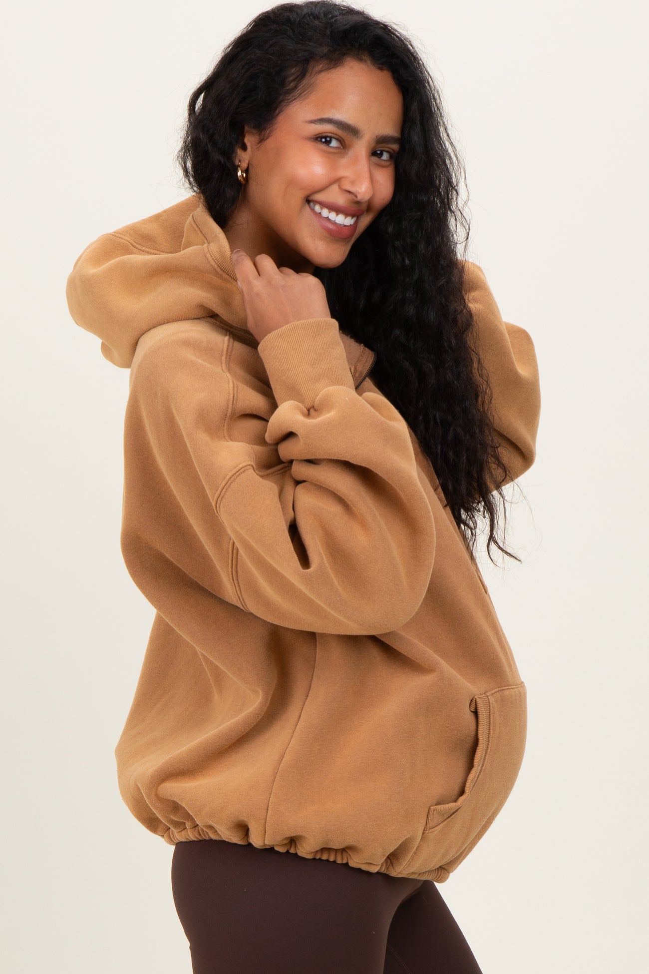 woman wearing a brown oversized maternity hoodie with a drawstring hood and pouch pocket, showing her baby bump