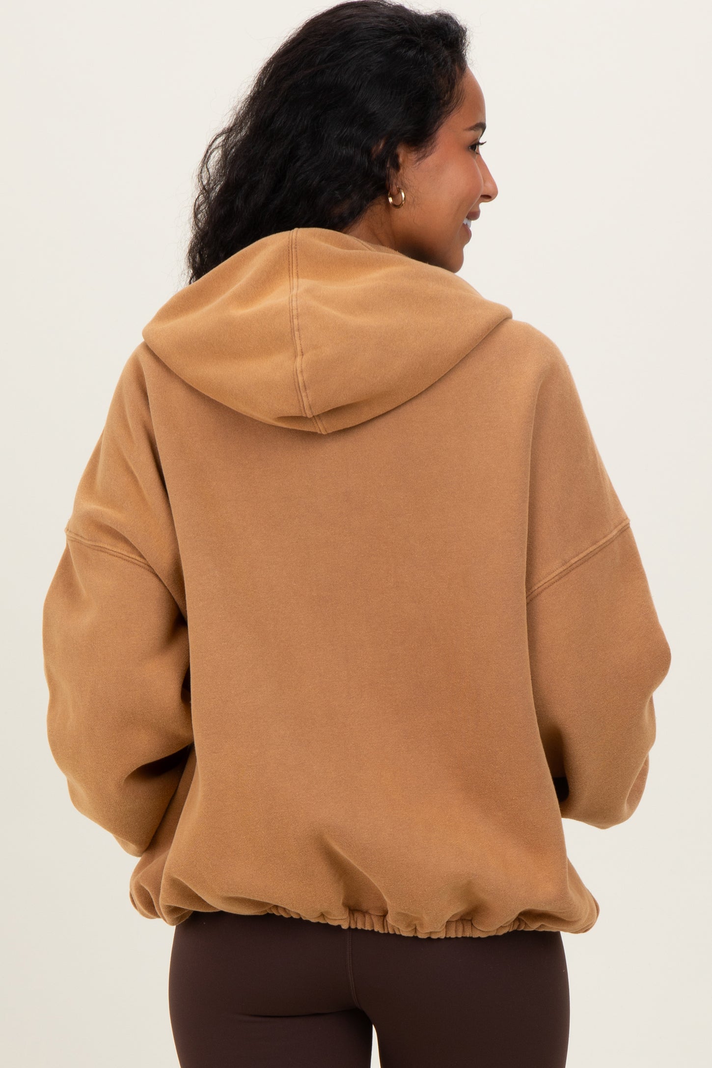 woman wearing a brown oversized hooded maternity sweatshirt with a cinched hem, showing her back
