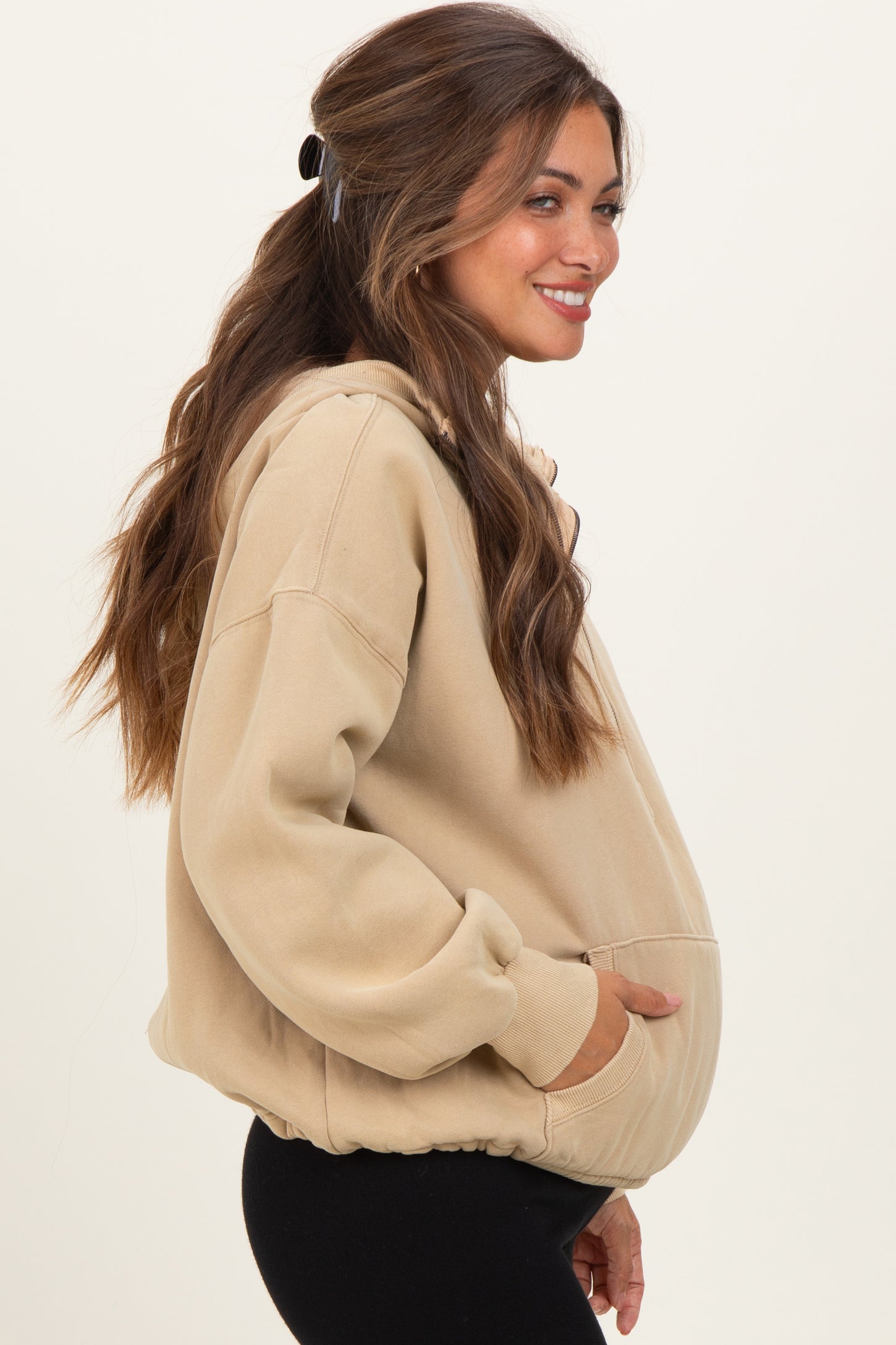 woman wearing a beige oversized maternity hoodie with pockets and a relaxed fit, showing a baby bump