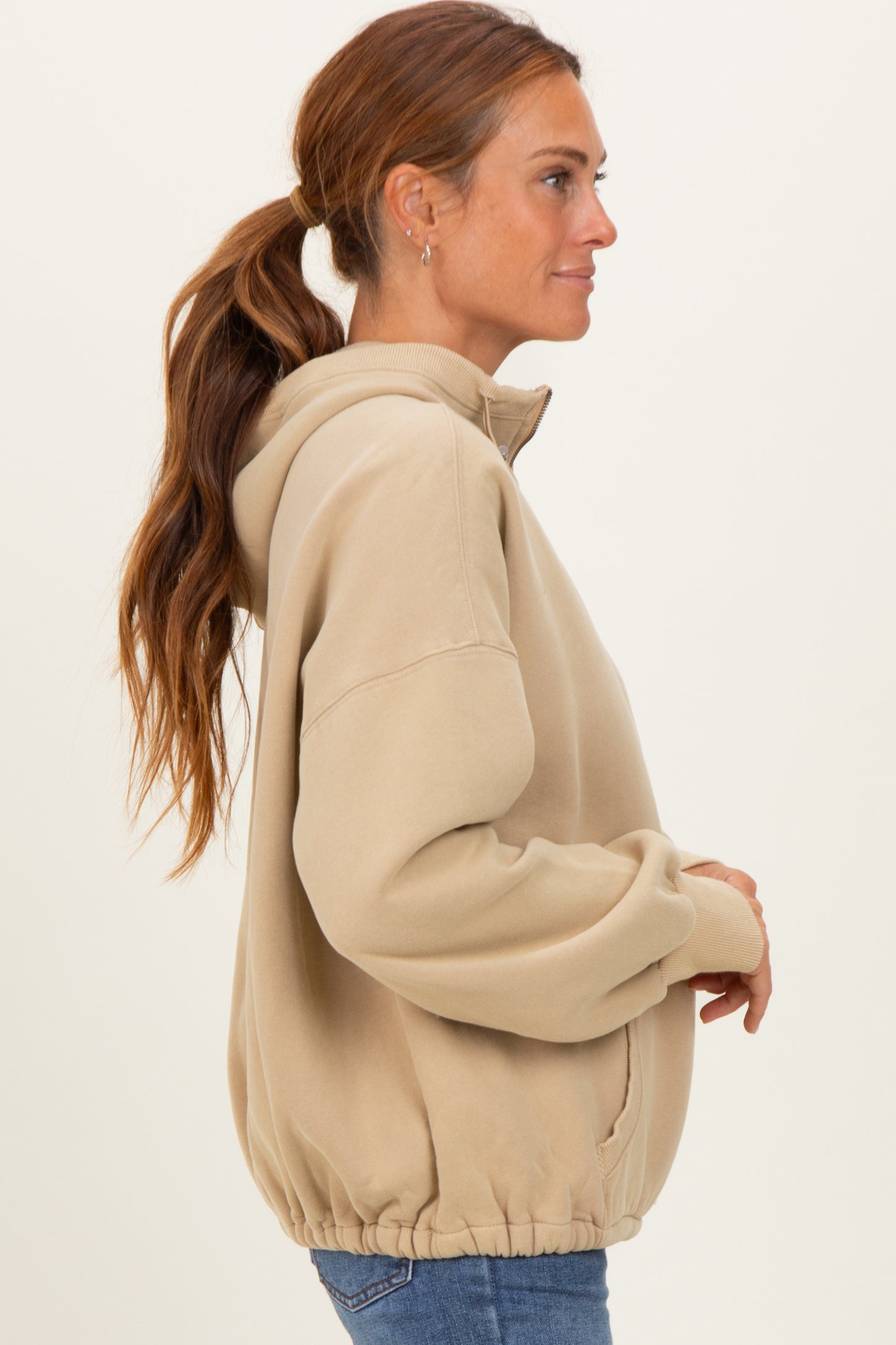 woman wearing a beige oversized hoodie with a half-zip and elastic hem, styled with blue jeans