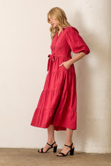 woman wearing a red wrap dress with puff sleeves and a tie belt, standing against a white wall