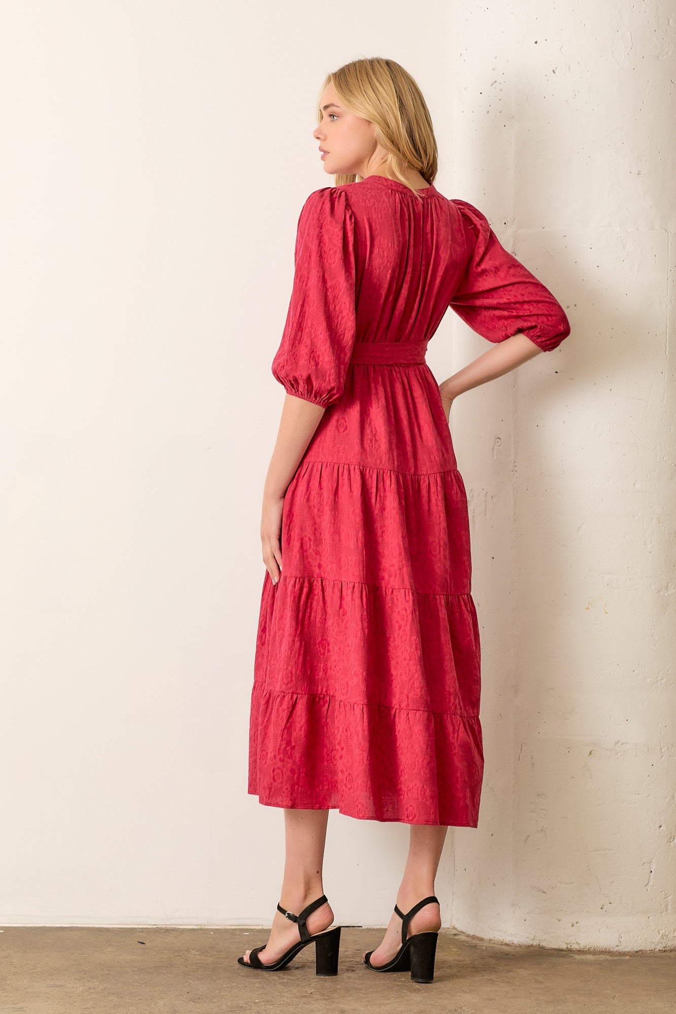 woman wearing a rose pink tiered midi dress with puff sleeves and a cinched waist, standing with her back to the camera