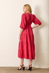 woman wearing a rose pink tiered midi dress with puff sleeves and a cinched waist, standing with her back to the camera