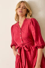 woman wearing a red textured midi dress with puff sleeves and a tie waist detail