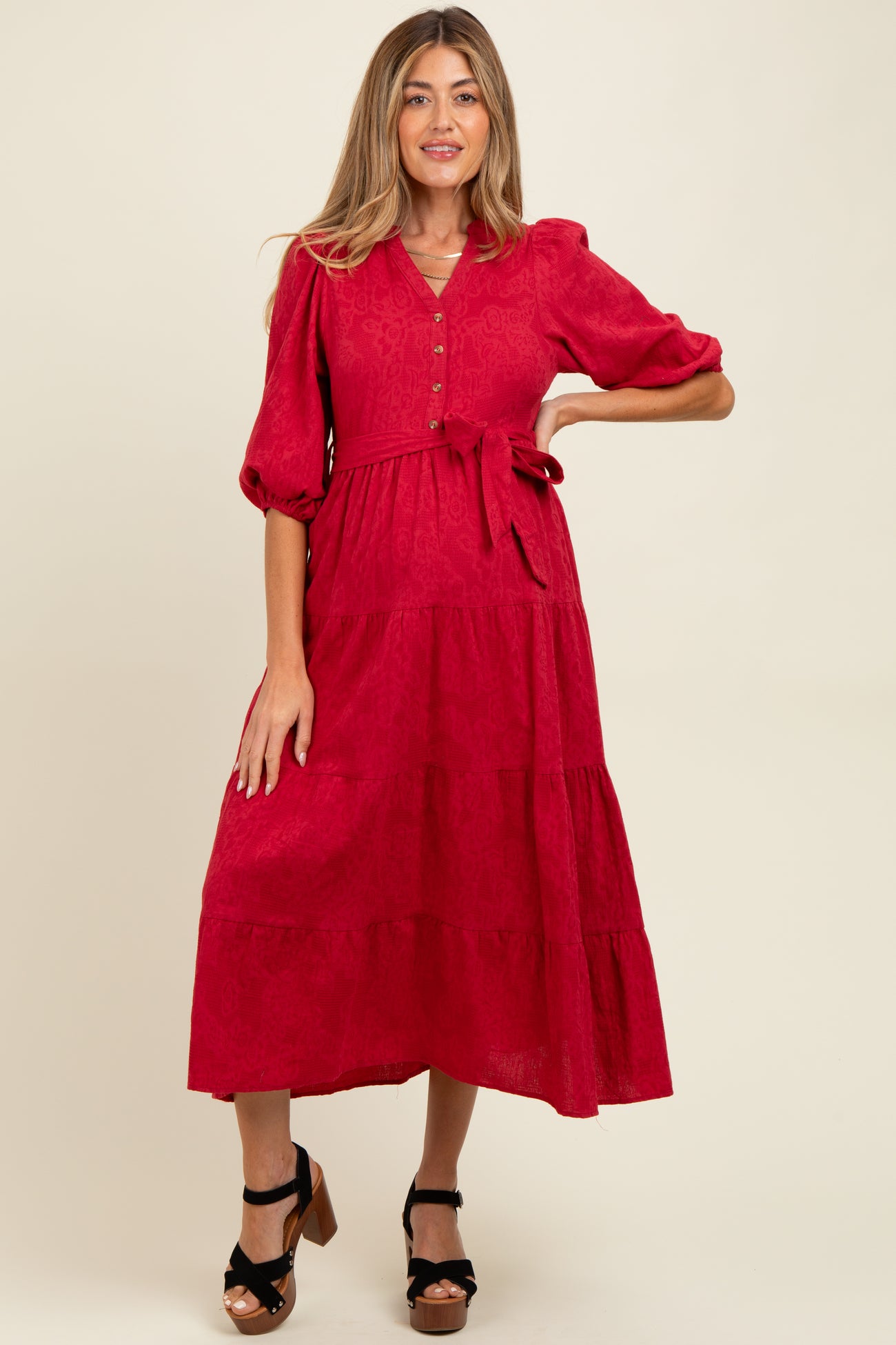 woman wearing a red maternity dress with puff sleeves, buttons, and a tied waist in a tiered design
