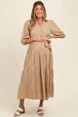 woman wearing a tan maternity midi dress with button details and a tie waist, showcasing her baby bump