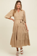 woman wearing a beige maternity dress with button detail, puff sleeves, and a tie waist, showcasing a baby bump