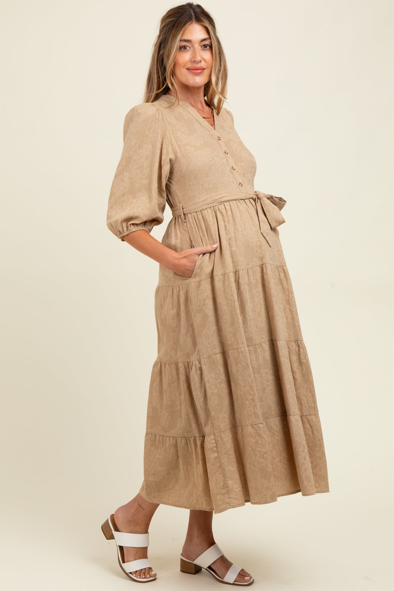 woman wearing a beige tiered maternity dress with buttons and puff sleeves, showing her baby bump