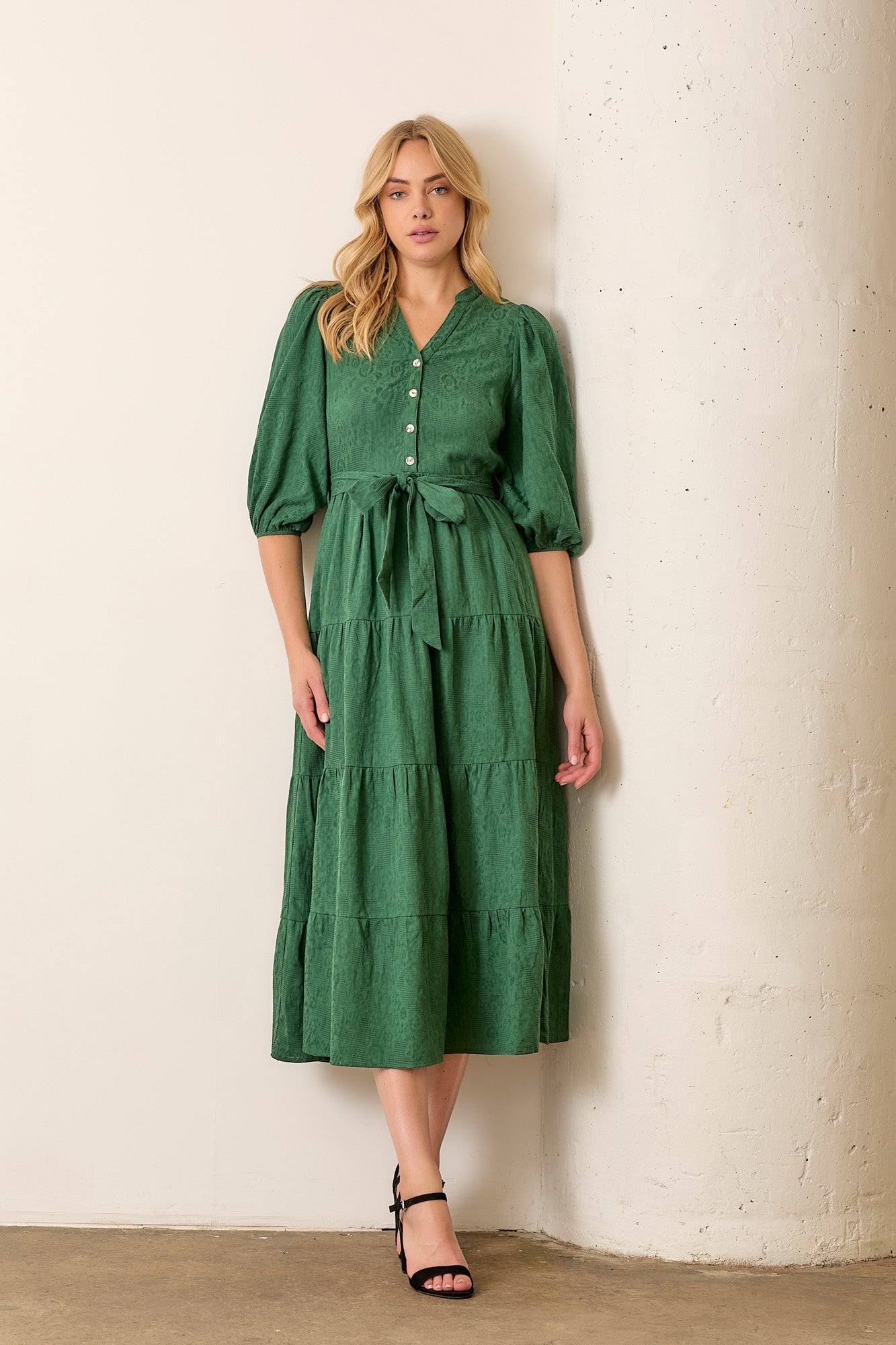 woman wearing a green tiered midi dress with puff sleeves, a button-down front, and a tie waist detail