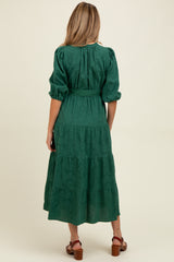 woman wearing a dark green maternity dress with puff sleeves and a tiered skirt, showing her baby bump from the back