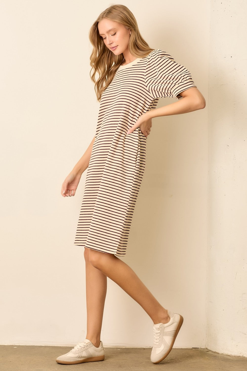 woman wearing a striped beige and brown oversized t-shirt dress with side pockets and white sneakers