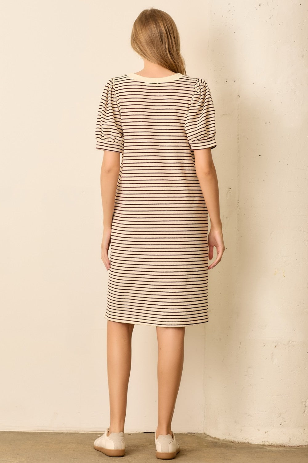 woman wearing a beige striped short sleeve dress with puff sleeves, standing with her back to the camera