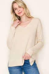 woman wearing a beige v-neck long sleeve top with ribbed texture and relaxed fit, paired with blue jeans