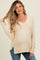 woman wearing a light beige maternity long sleeve top with a v-neck and side slits, showcasing her baby bump