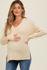woman wearing a beige long sleeve maternity top with a v-neck and holding her baby bump