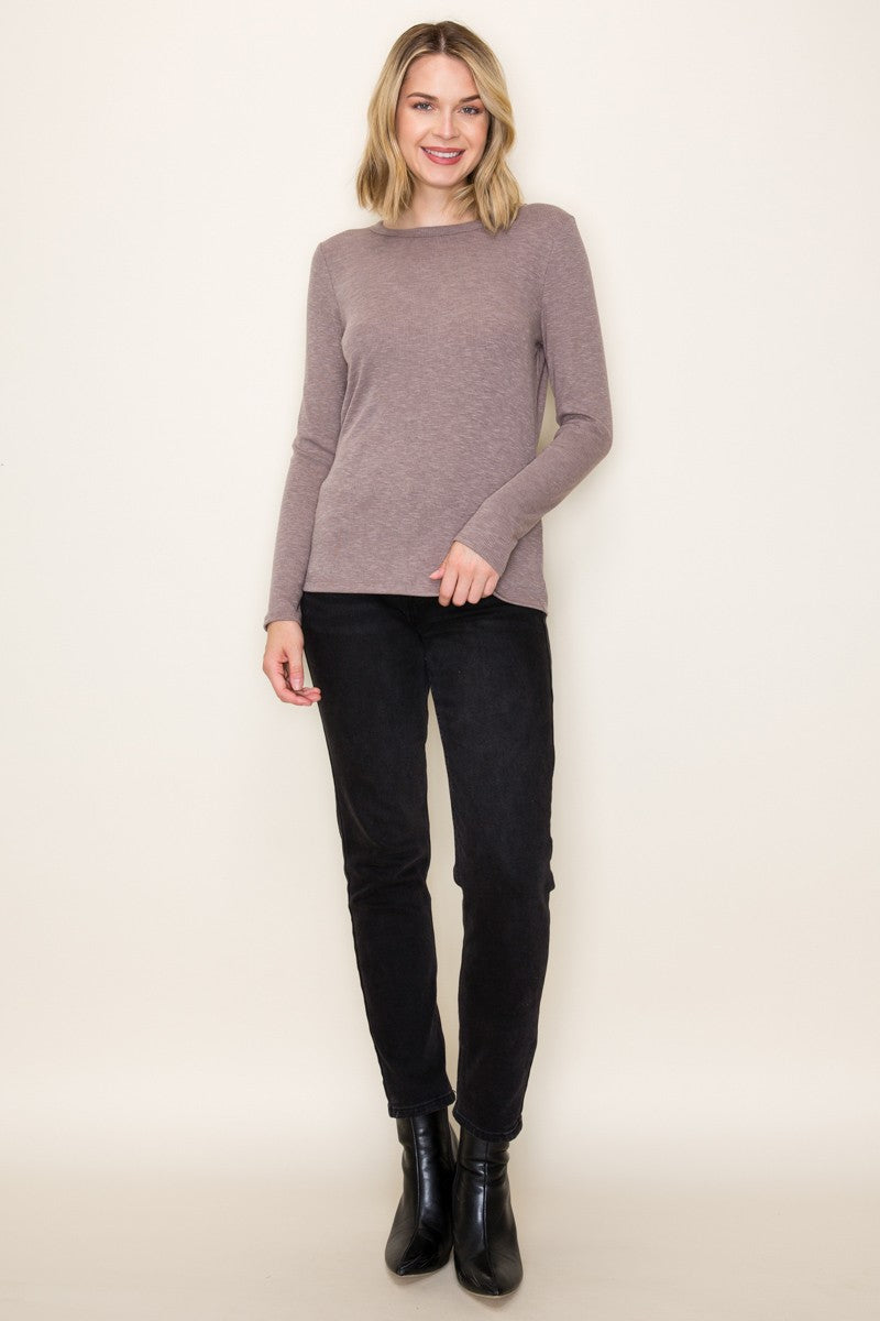 woman wearing a taupe long sleeve sweater and black skinny pants, standing against a light background