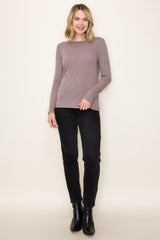 woman wearing a taupe long sleeve sweater and black skinny pants, standing against a light background