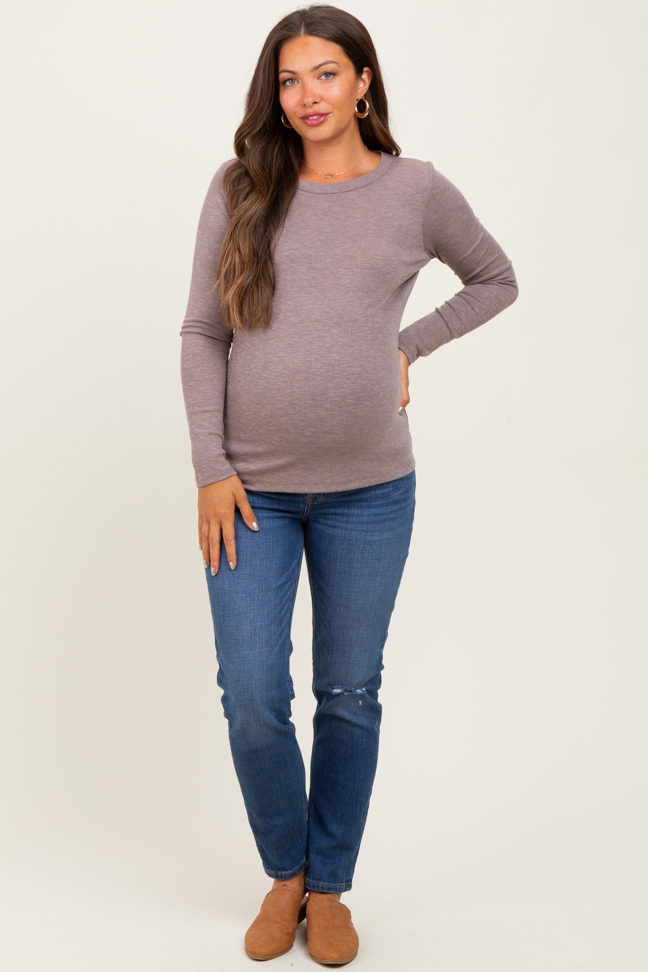 woman wearing a brown long sleeve maternity top and blue jeans, showing her baby bump