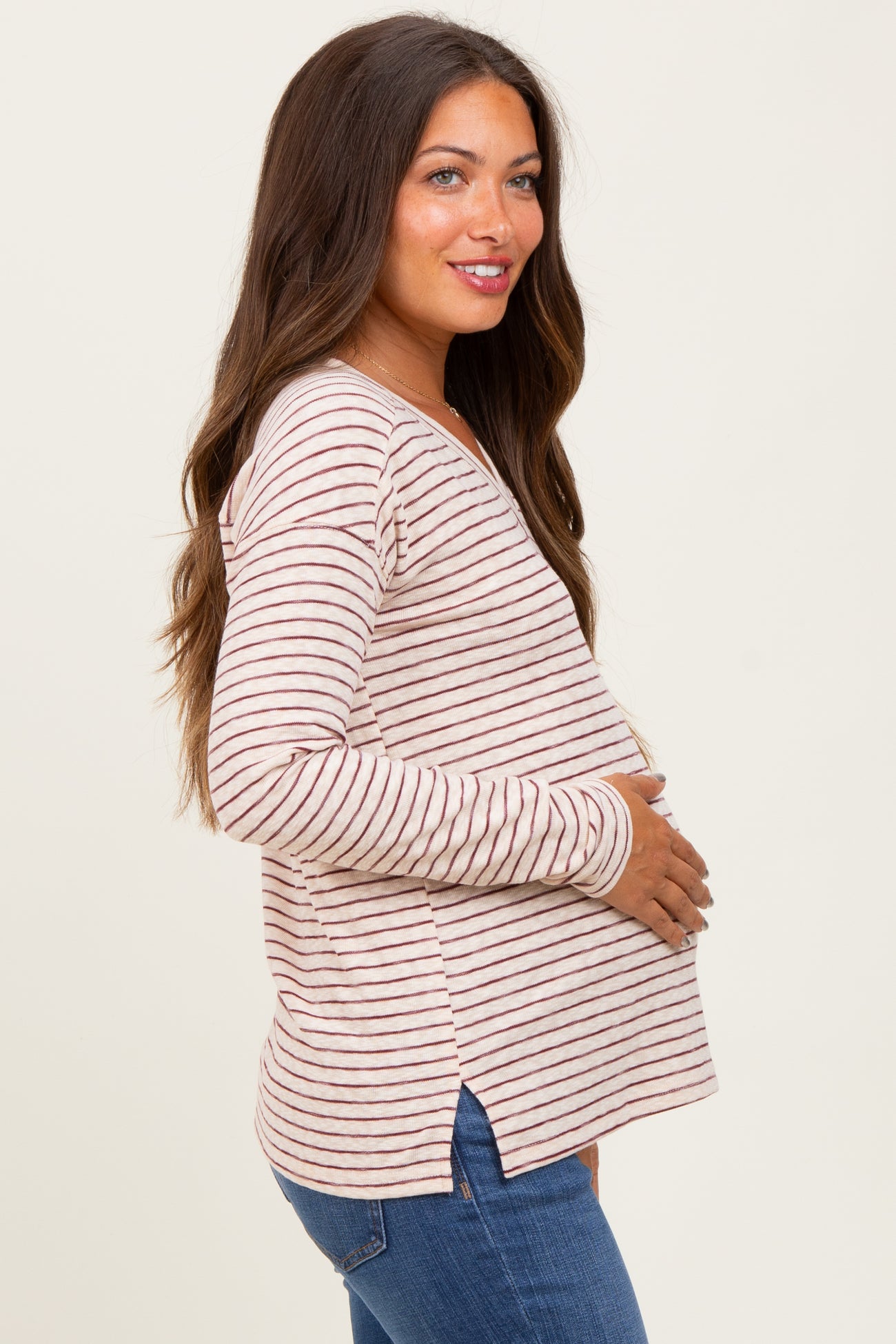 woman wearing a light pink and white striped maternity top with a v-neck and side slits, holding her baby bump