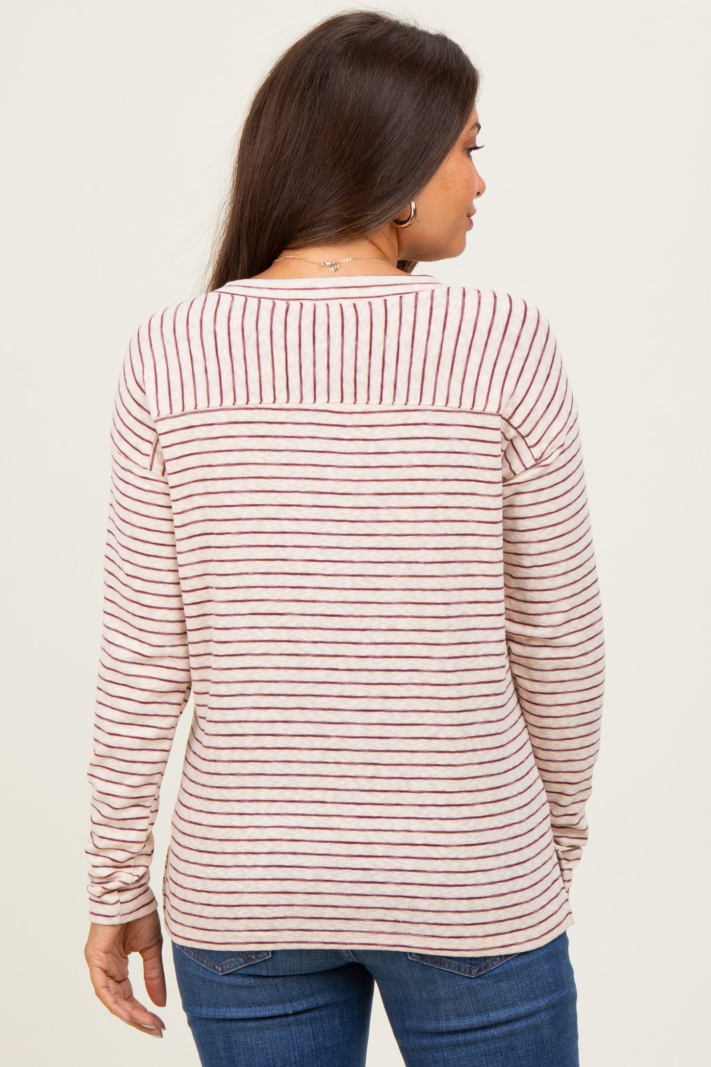 woman wearing a striped maternity top with long sleeves, showing the back view and soft pink and burgundy colors