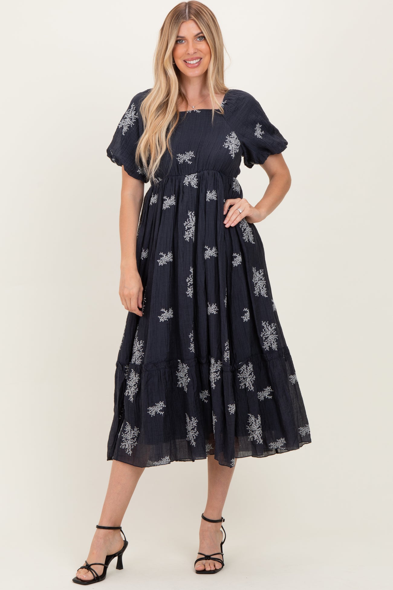 woman wearing a navy blue embroidered midi dress with short puff sleeves and a tiered skirt, styled with black heels