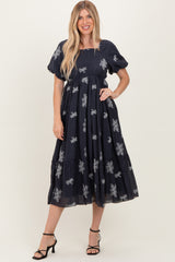 woman wearing a navy blue embroidered midi dress with short puff sleeves and a tiered skirt, styled with black heels
