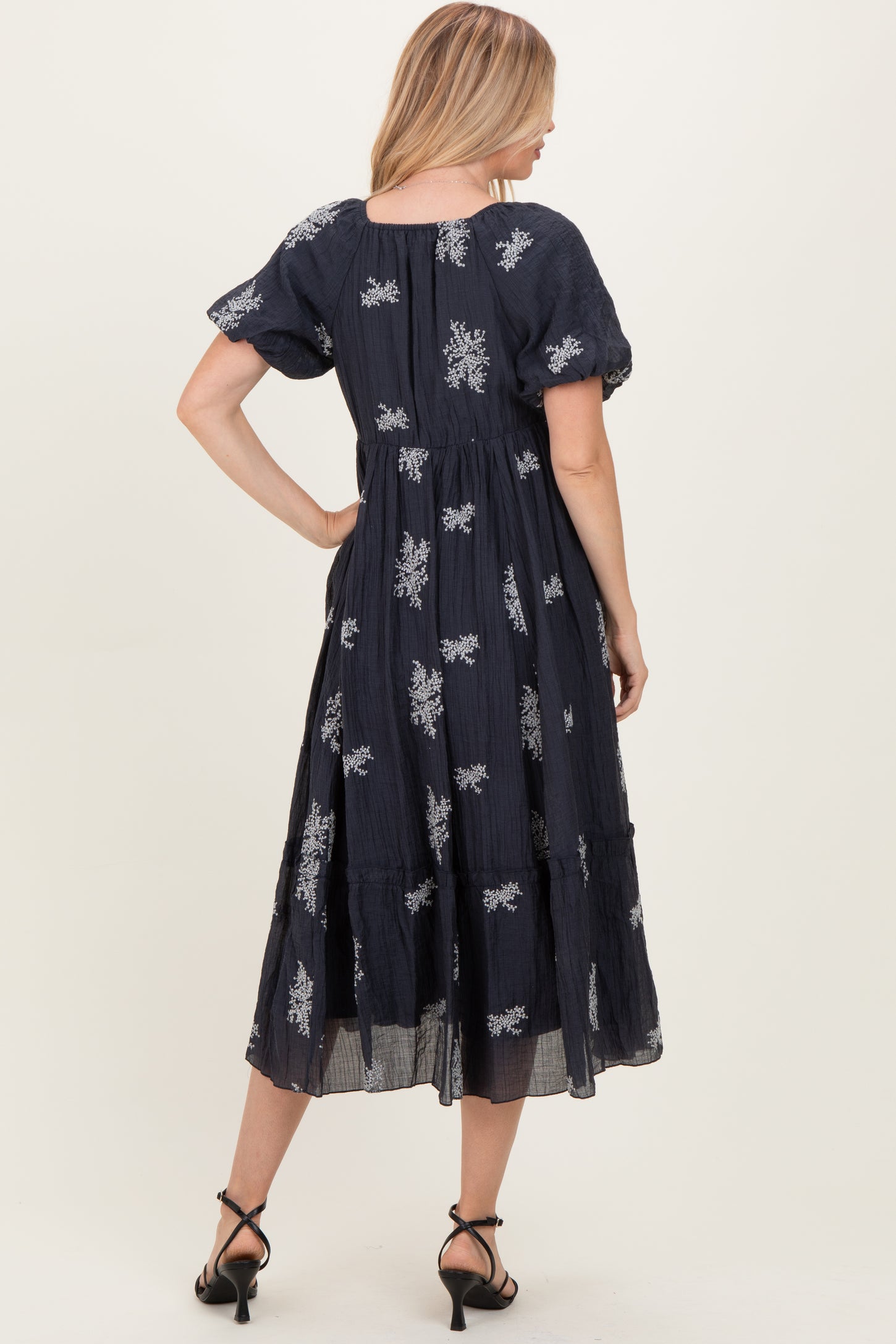 woman wearing a navy blue embroidered midi dress with short puff sleeves and a tiered skirt